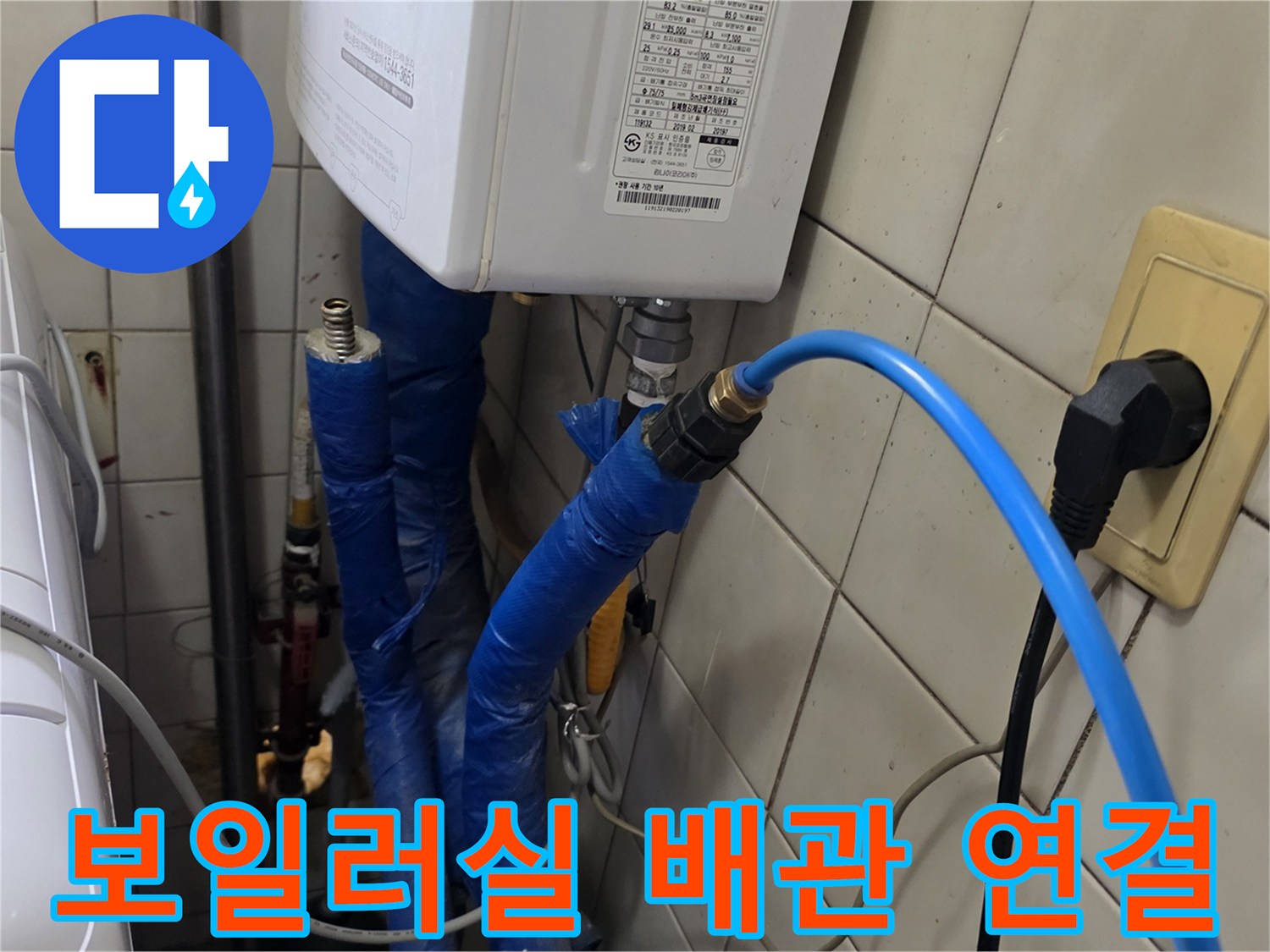 파란색 호스로 연결된 보일러 하단 배관과 타일 벽면