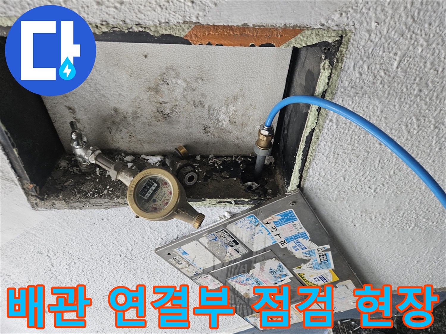 벽면 내부에 노출된 배관 부속과 계량기를 점검하는 장면입니다.