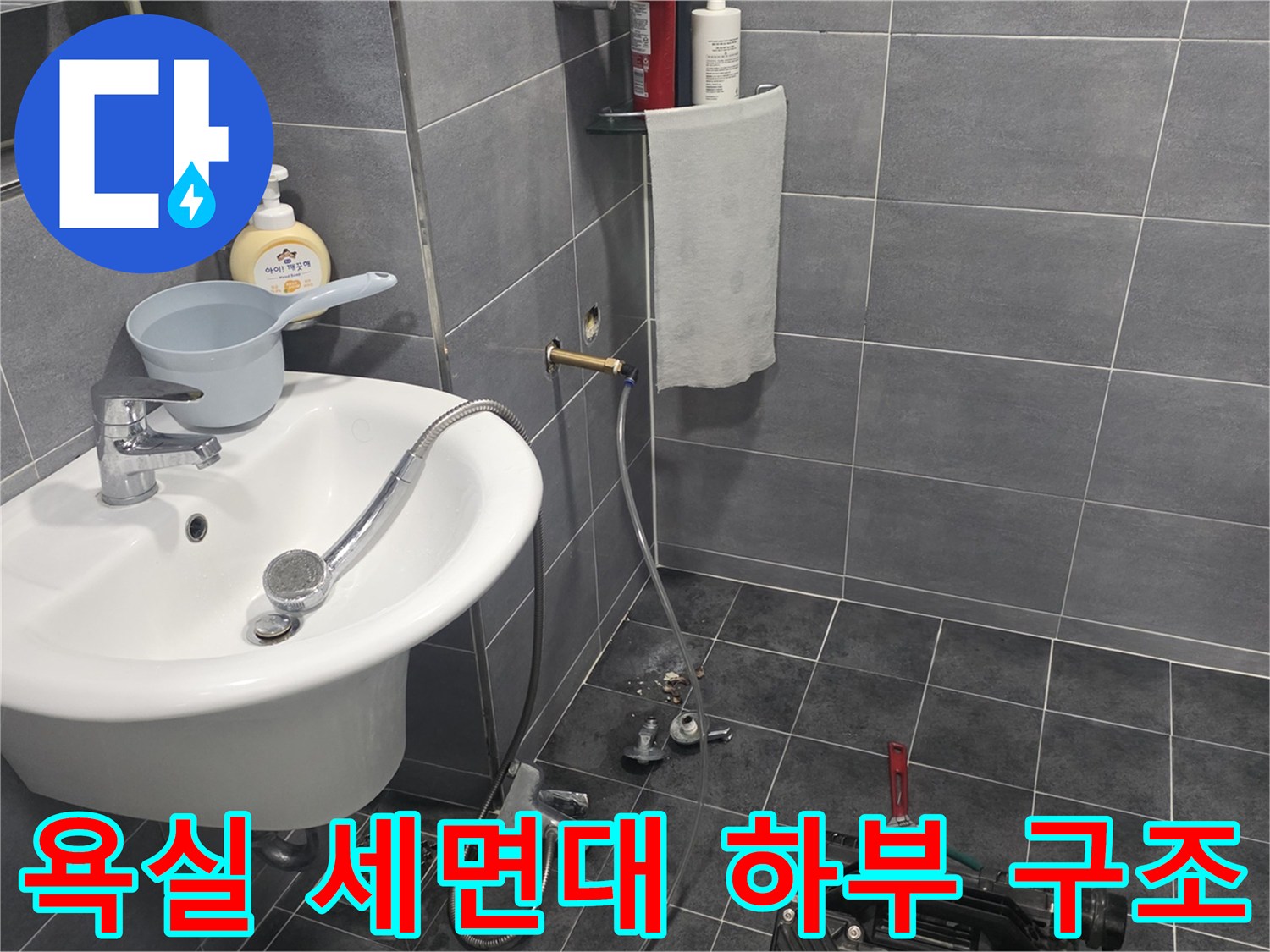 회색 타일 벽면과 세면대 아래의 금속 수전 부품