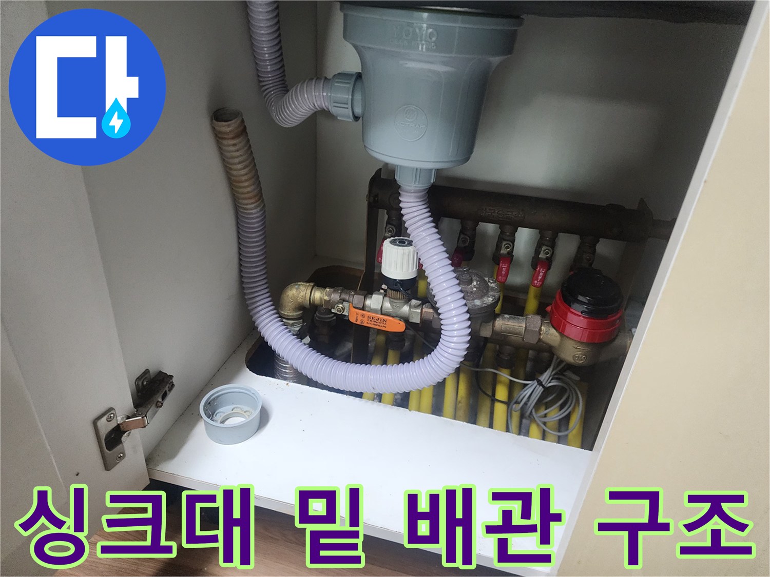 싱크대 하부장 내부의 회색 주름관과 다수의 배수 분기점