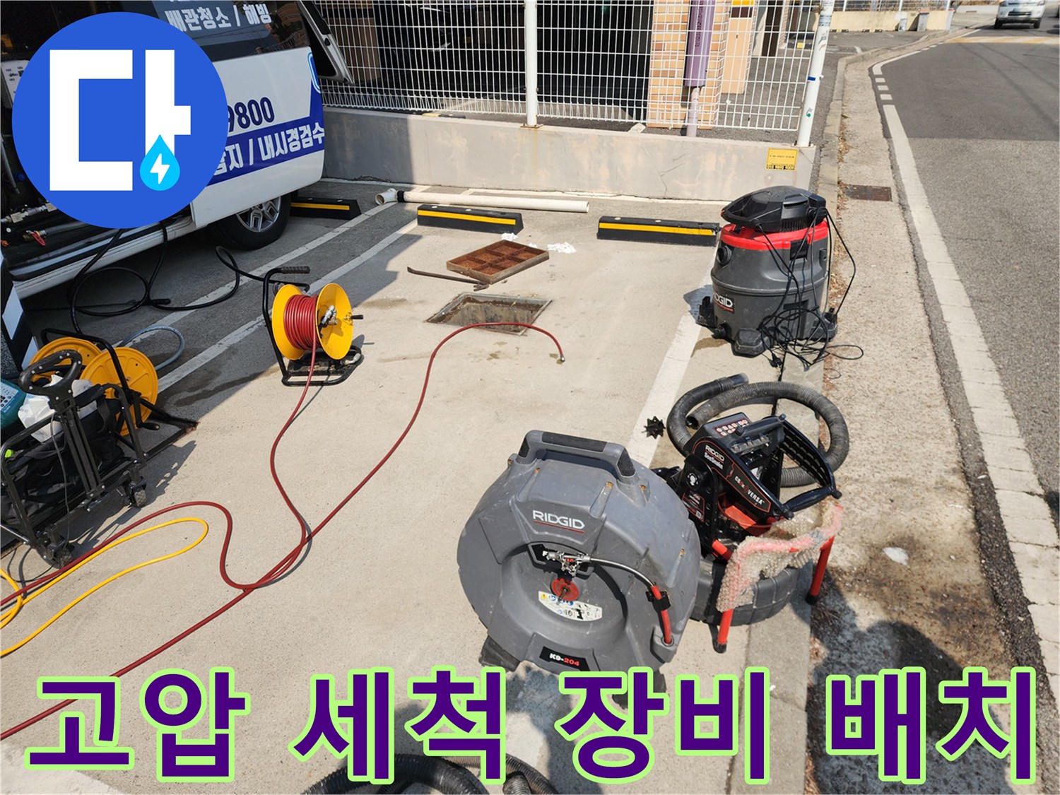 야외 맨홀 부근에 놓인 고압 호스 릴과 산업용 집수정 청소기