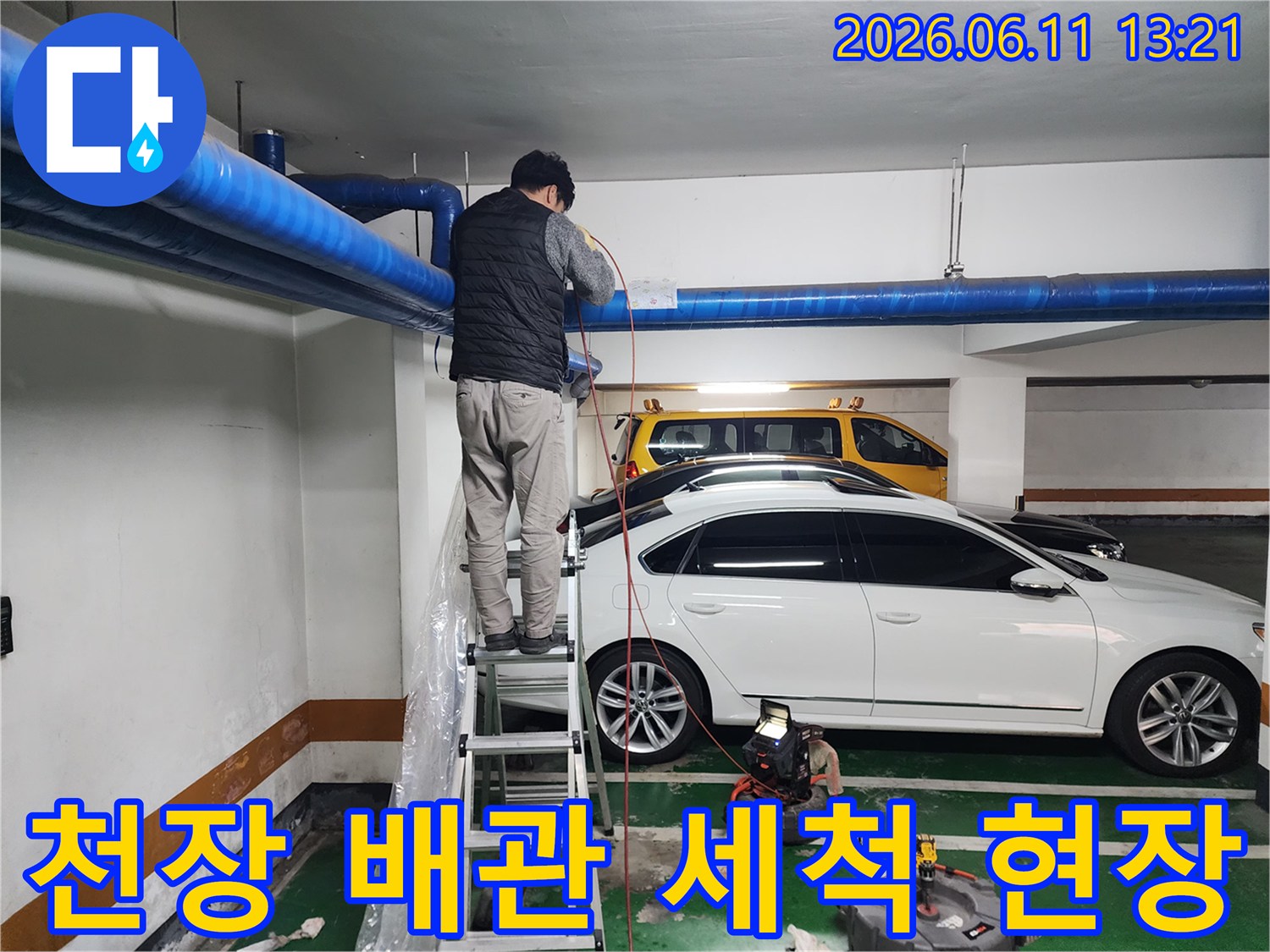 지하주차장 천장의 파란색 대형 배관을 청소하는 작업 모습입니다.