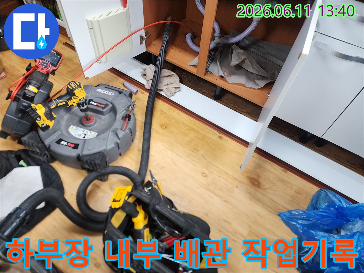 싱크대 아래쪽 하부장 배관과 작업용 장비들이 놓여 있는 현장 사진입니다.