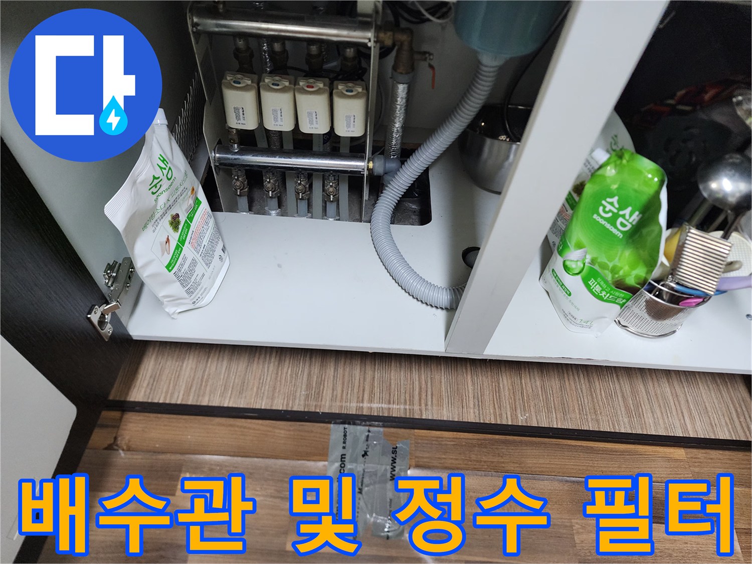 싱크대 하단에 설치된 정수기 필터와 회색 배수 호스입니다.