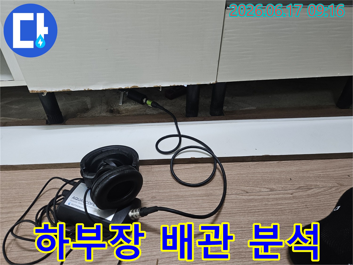 누수 탐지 장비의 센서가-싱크대 하부장 틈새에 삽입되어-배관의 누수음을 정밀하게 분석하는 모습