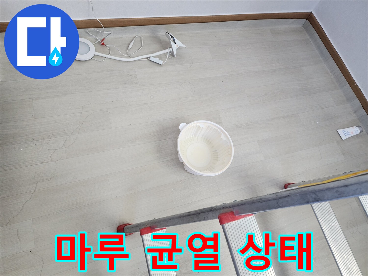 바닥 마루재의 갈라짐 부위와 작업용 사다리 일부가 보이는 현장 사진