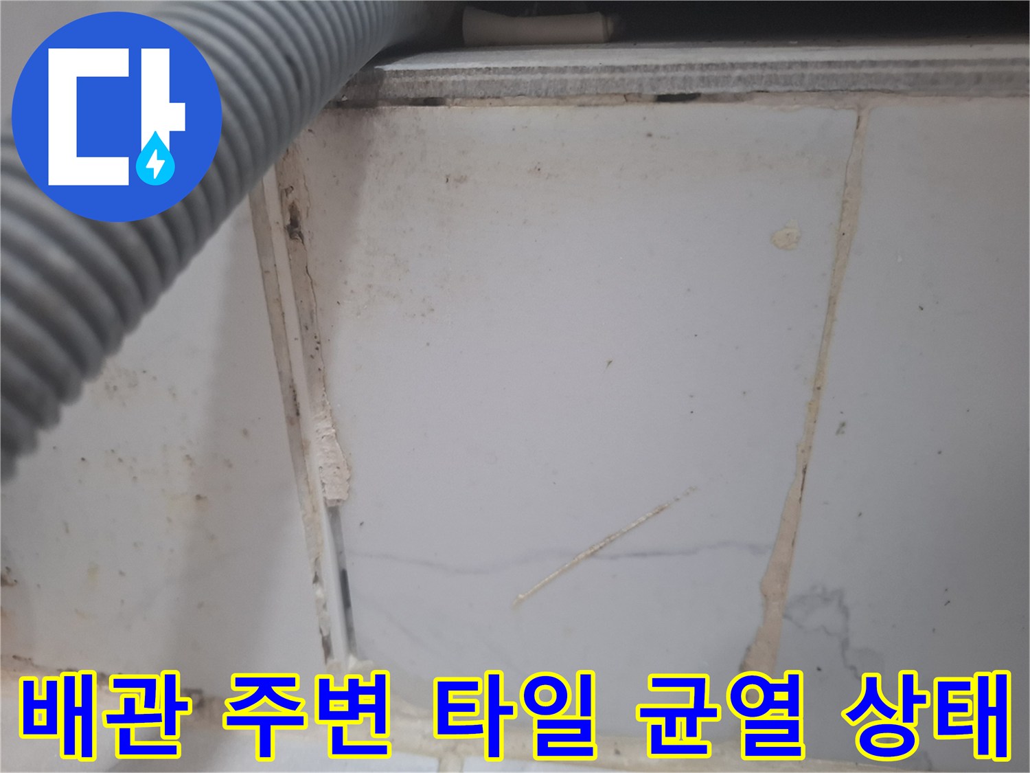 갈라진 타일 틈새와 회색 주름관 노출