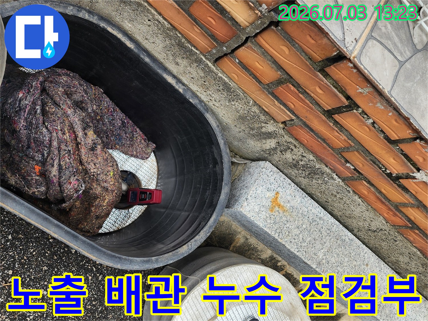 오렌지 타일 벽면에 인접한 노출된 수도배관 보수 현장
