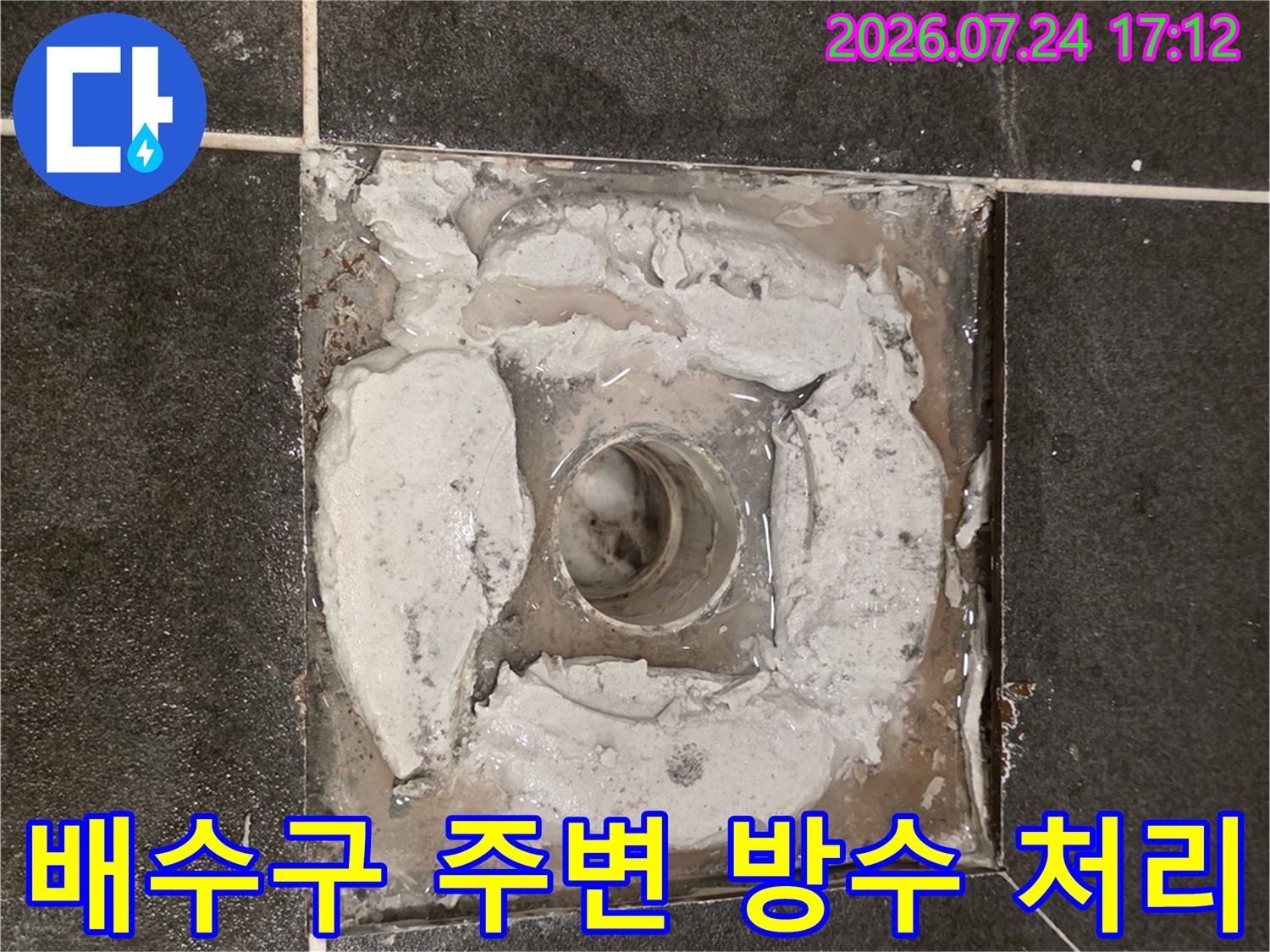배수구 주변의 노출된 배관과 젖은 시멘트 마감 부위