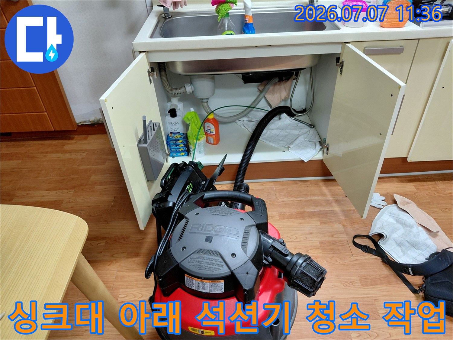 석션 기계를 연결하여 싱크대 하부 배관의 찌꺼기를 흡입하는 전문적인 모습
