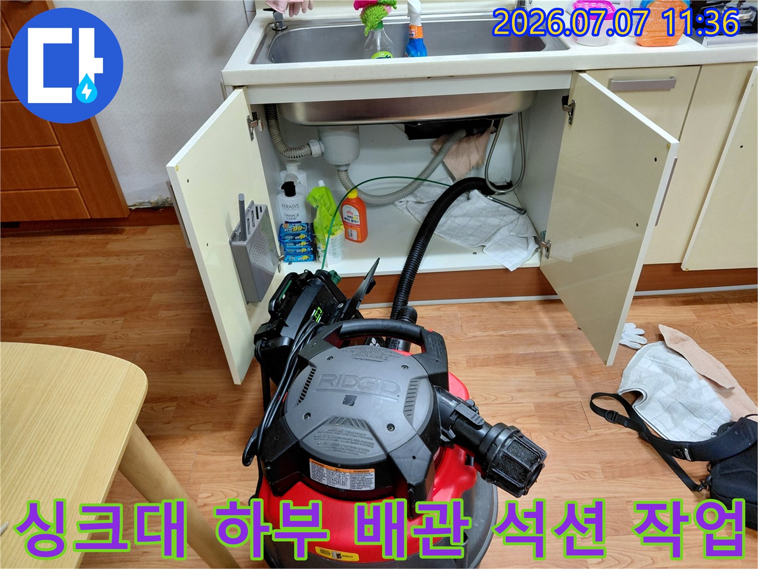 싱크대 아래 공간에서 강력한 석션 장비를 사용하여 배관 속 오물을 제거하는 모습