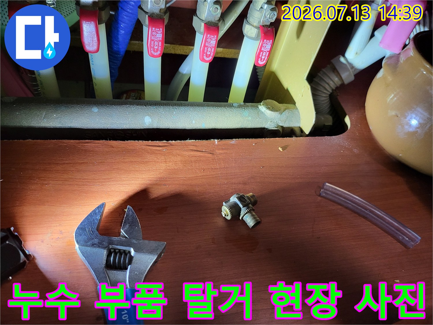 배관 연결용 티자 모양의 황동 부속과 몽키스패너가 바닥에 놓여있는 모습
