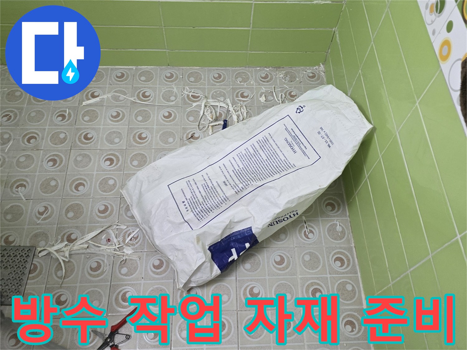 욕실 타일 위에 놓인 흰색 포대와 공구류