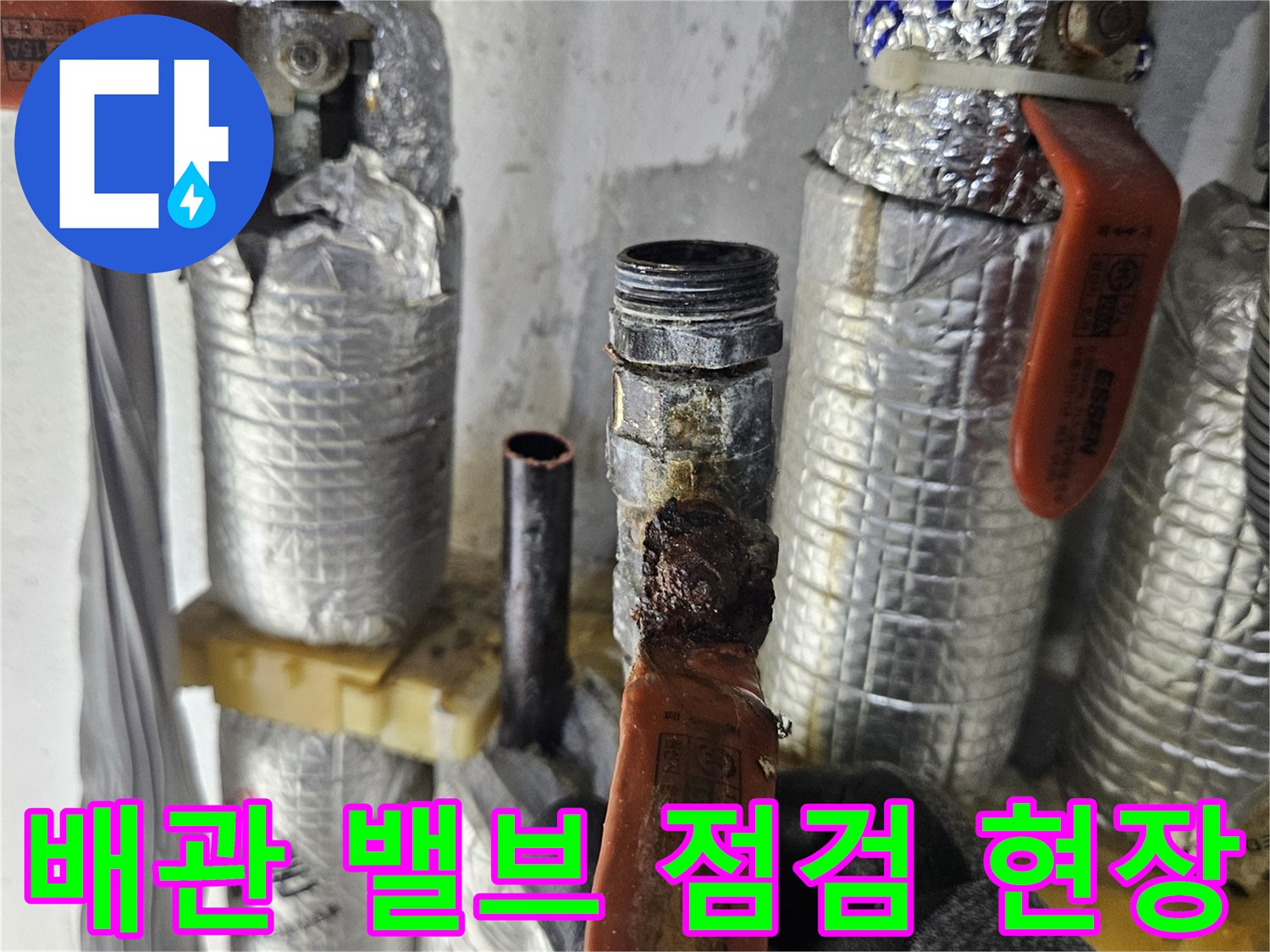 은박 보온재로 감싸진-배관과 주황색 밸브의 모습입니다.