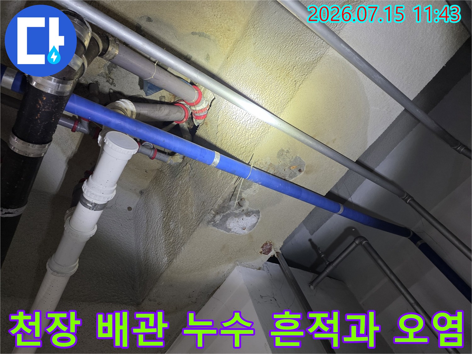 콘크리트 천장에 설치된 파란색과 흰색 배관 주변으로 노란색 누수 얼룩이 퍼져 있는 모습