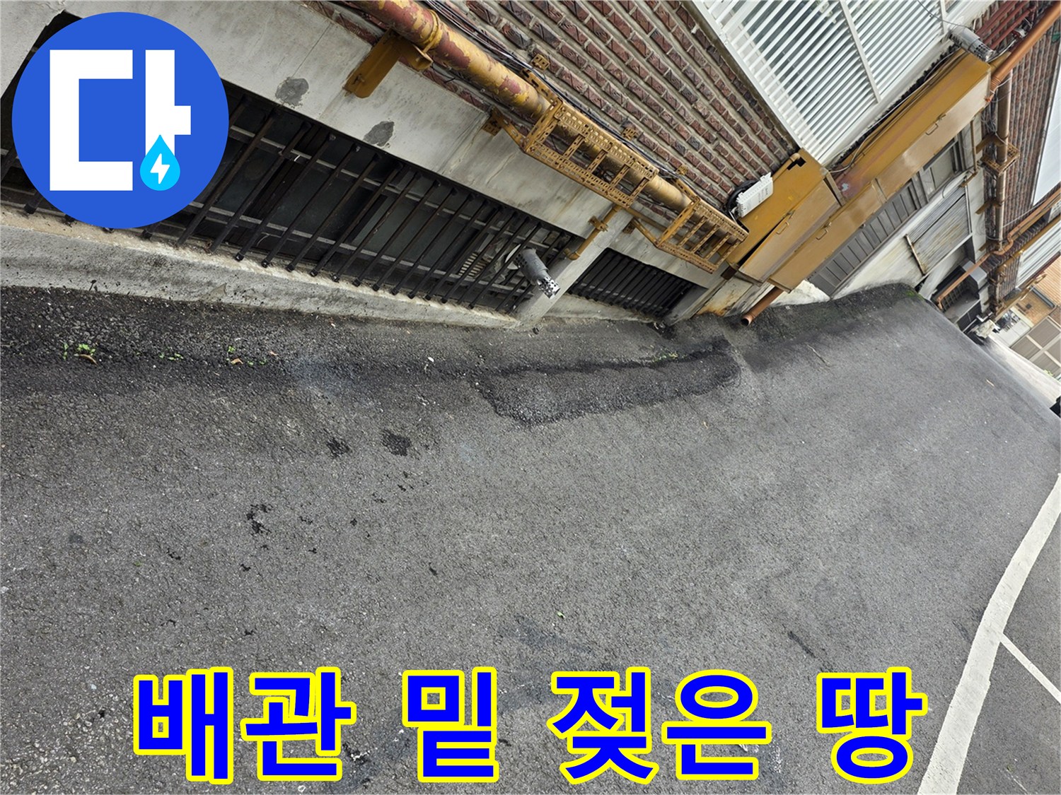 건물 외벽 배관 아래 아스팔트의 어두운 습기 자국