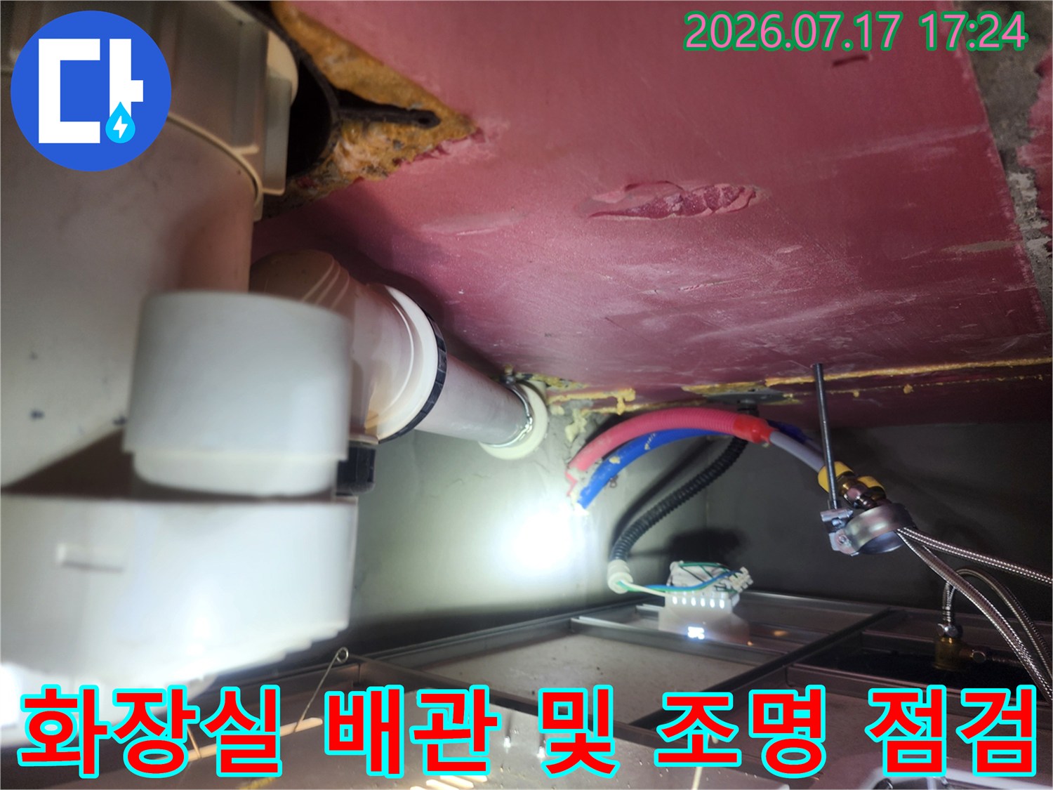 어두운 천장 내부에 조명을 켜고 배수 파이프를 세밀하게 관찰하는 모습