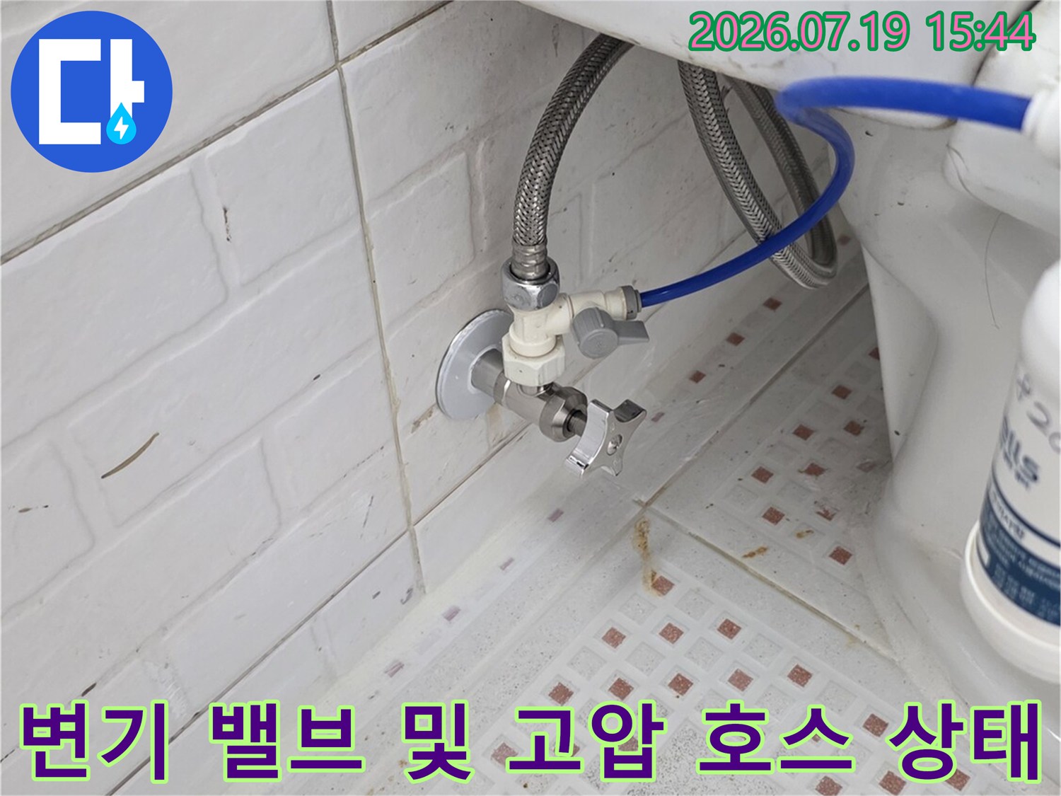 흰색 타일 벽면에 설치된 변기용 급수 앵글밸브와 파란색 연결 호스