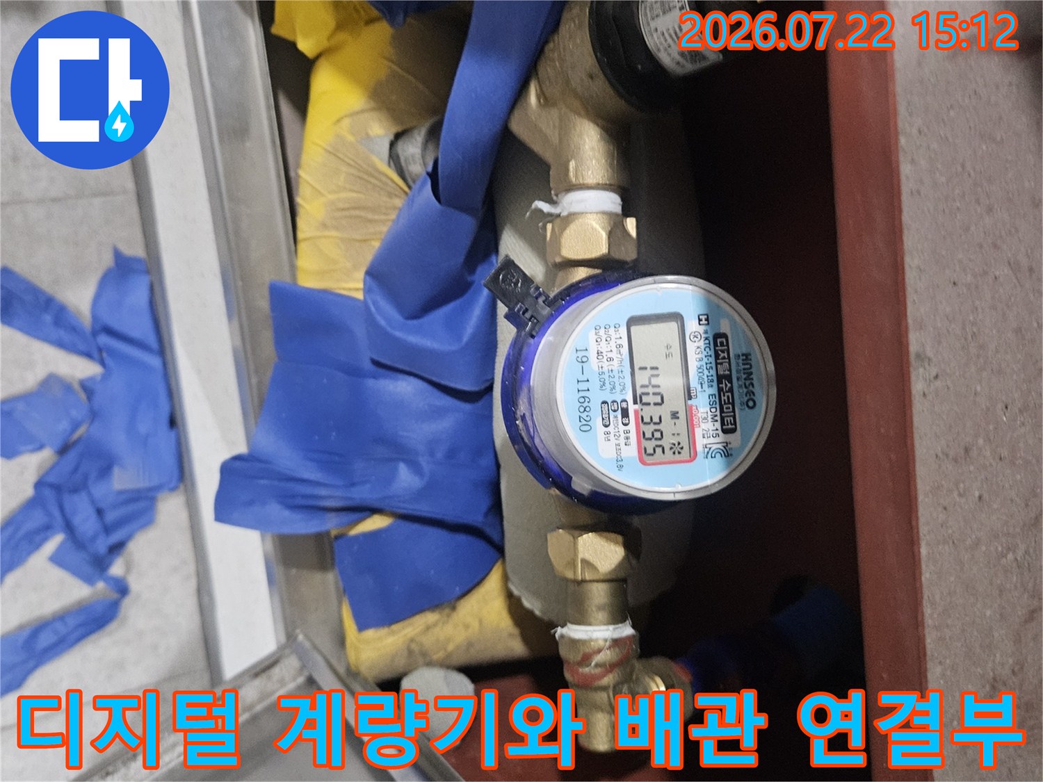 금속제 밸브와 디지털 수도 계량기가 연결되어 있으며 하단은 파란색 천으로 보양된 모습