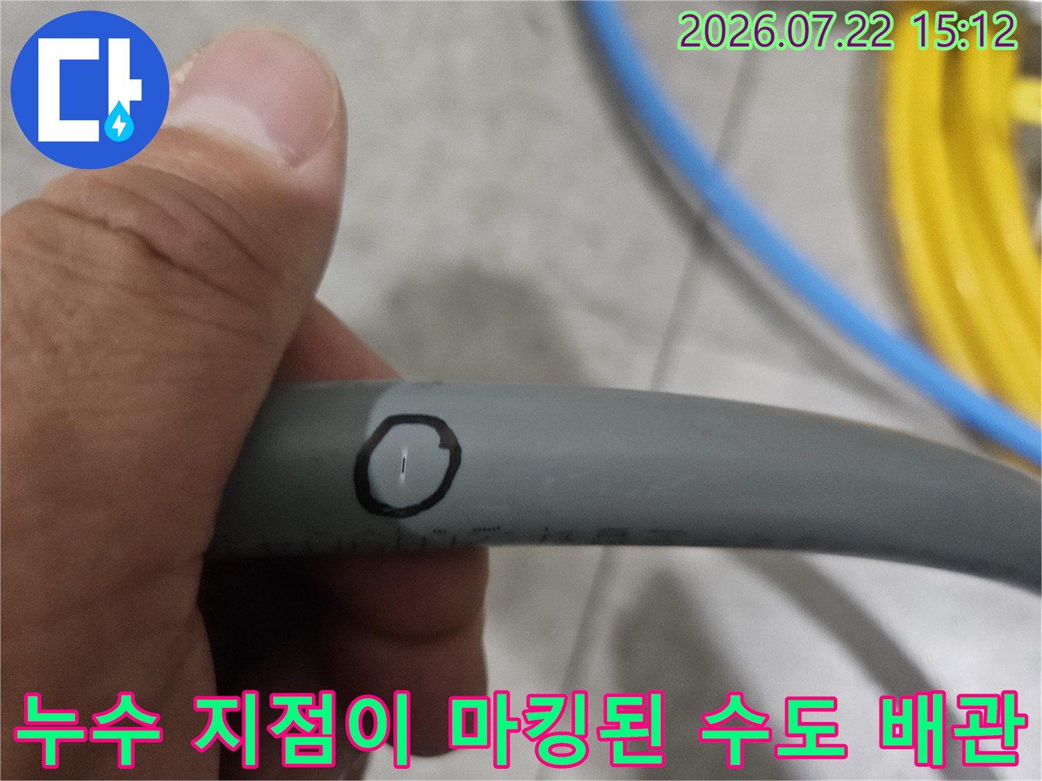 손으로 잡고 있는 회색 플라스틱 배관의 특정 부위에 누수 지점을 표시한 사진