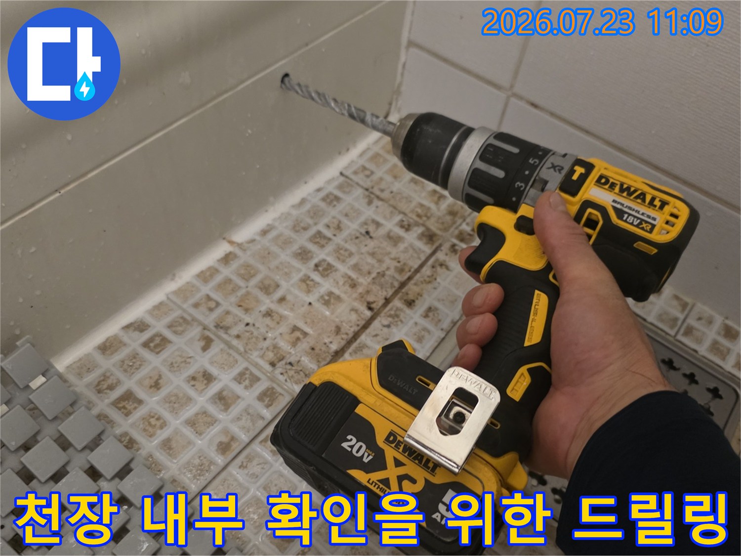 전동드릴 장비를 손에 쥐고 천장의 타일 접합 부위를 뚫고 있는 모습