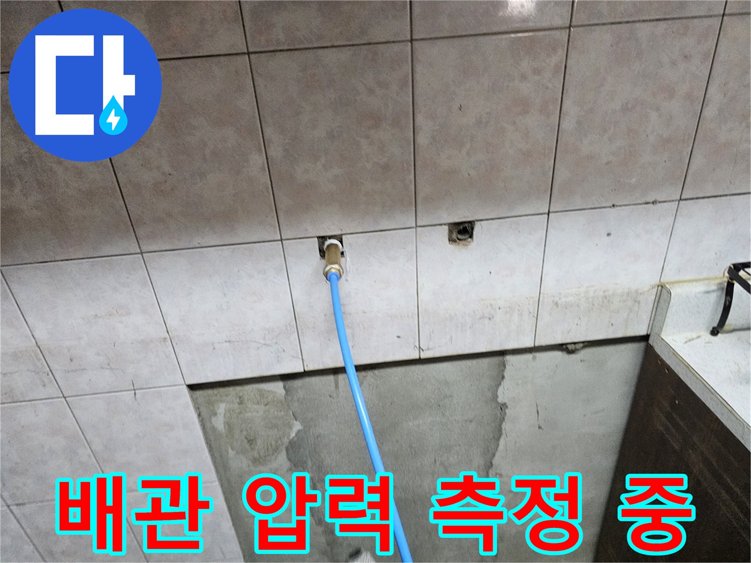 타일 벽면 돌출 배관에-파란색 호스가 연결된 모습