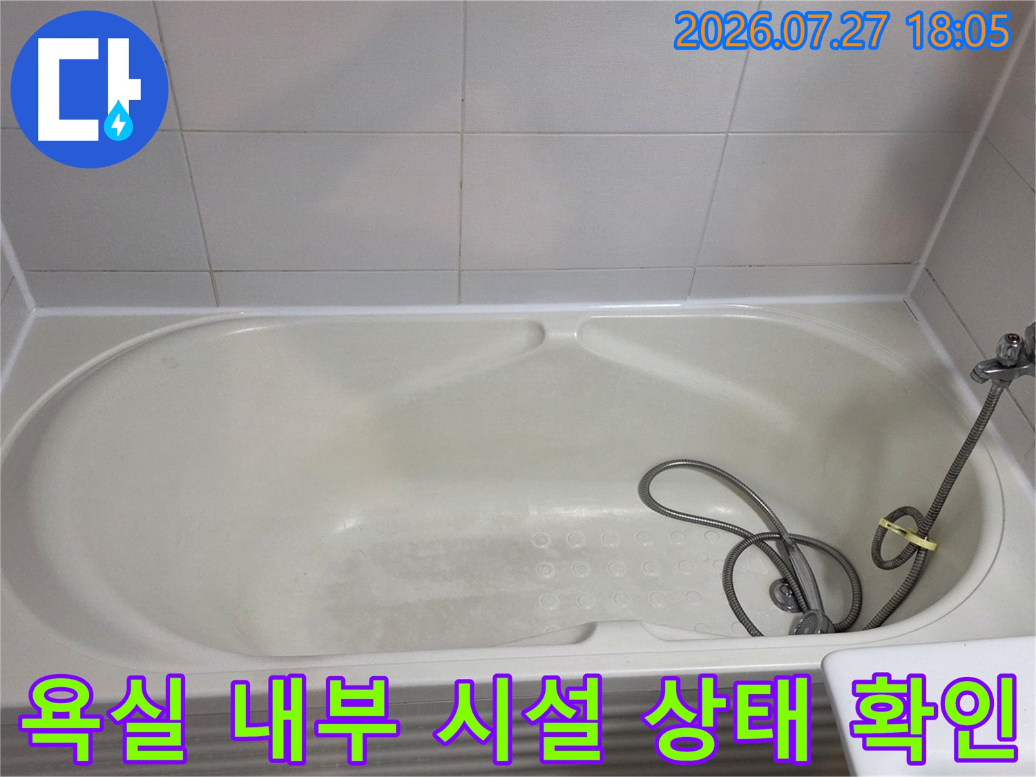 샤워 호스가 놓여 있는 흰색 욕조와 베이지색 벽면 타일 사진
