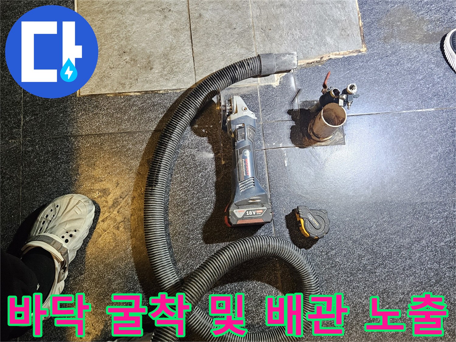 검은색 타일 바닥을 파낸 후 드러난 손상된 수도 배관과 공구