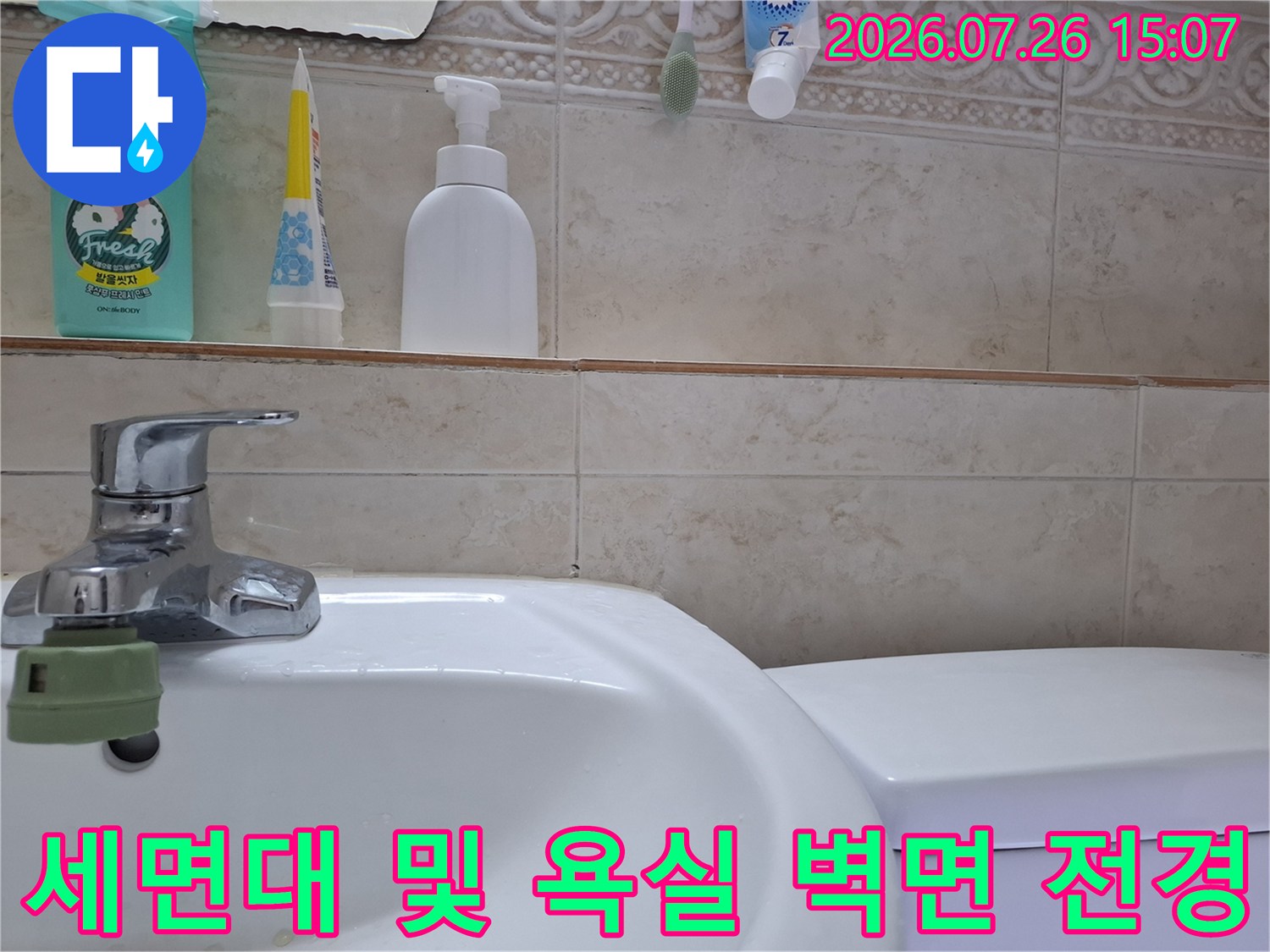금속제 세면대 수전과 베이지색 타일-선반 위에 놓인 화장품 용기들