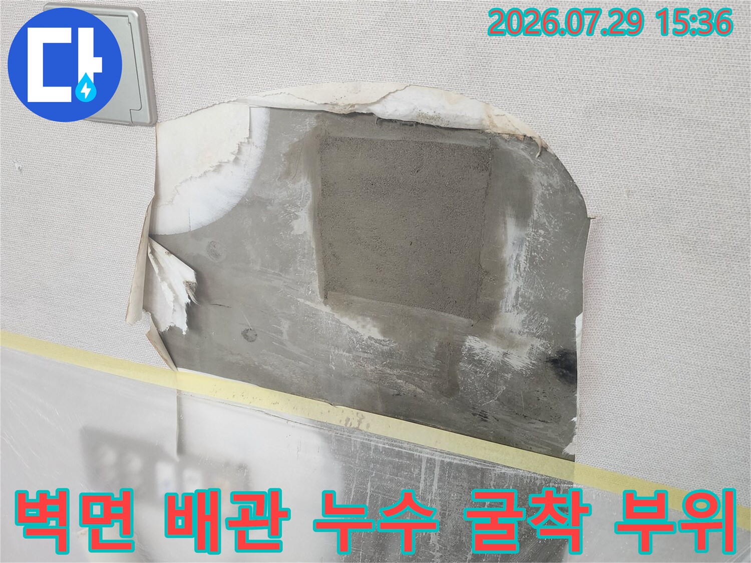 벽지 안쪽을 파내어 노출된 회색 배관과 수리 전 상태를 보여주는 현장 사진