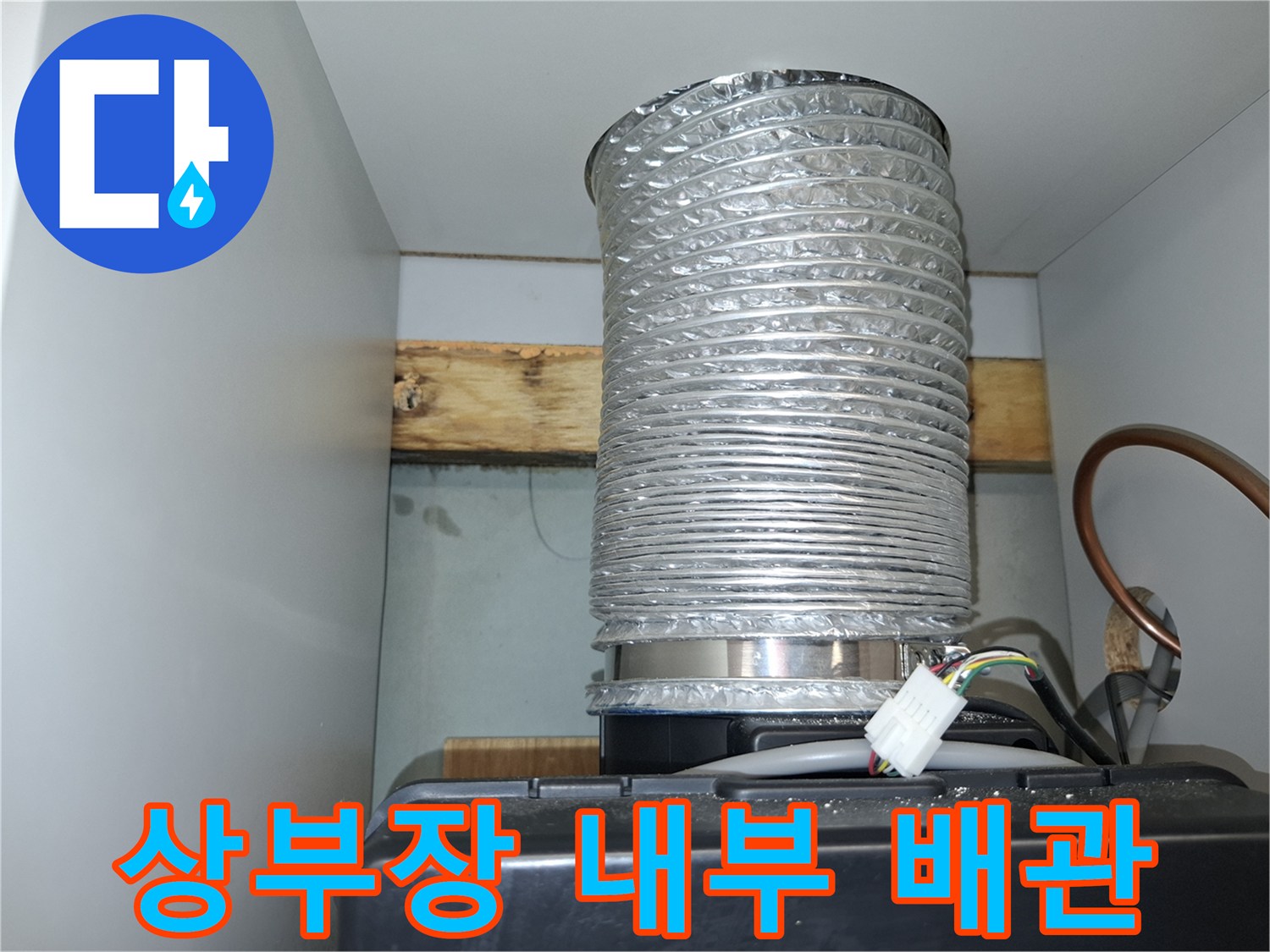 주방 상부장 내부에 노출된 은색 배수 호스 및 배선 구조