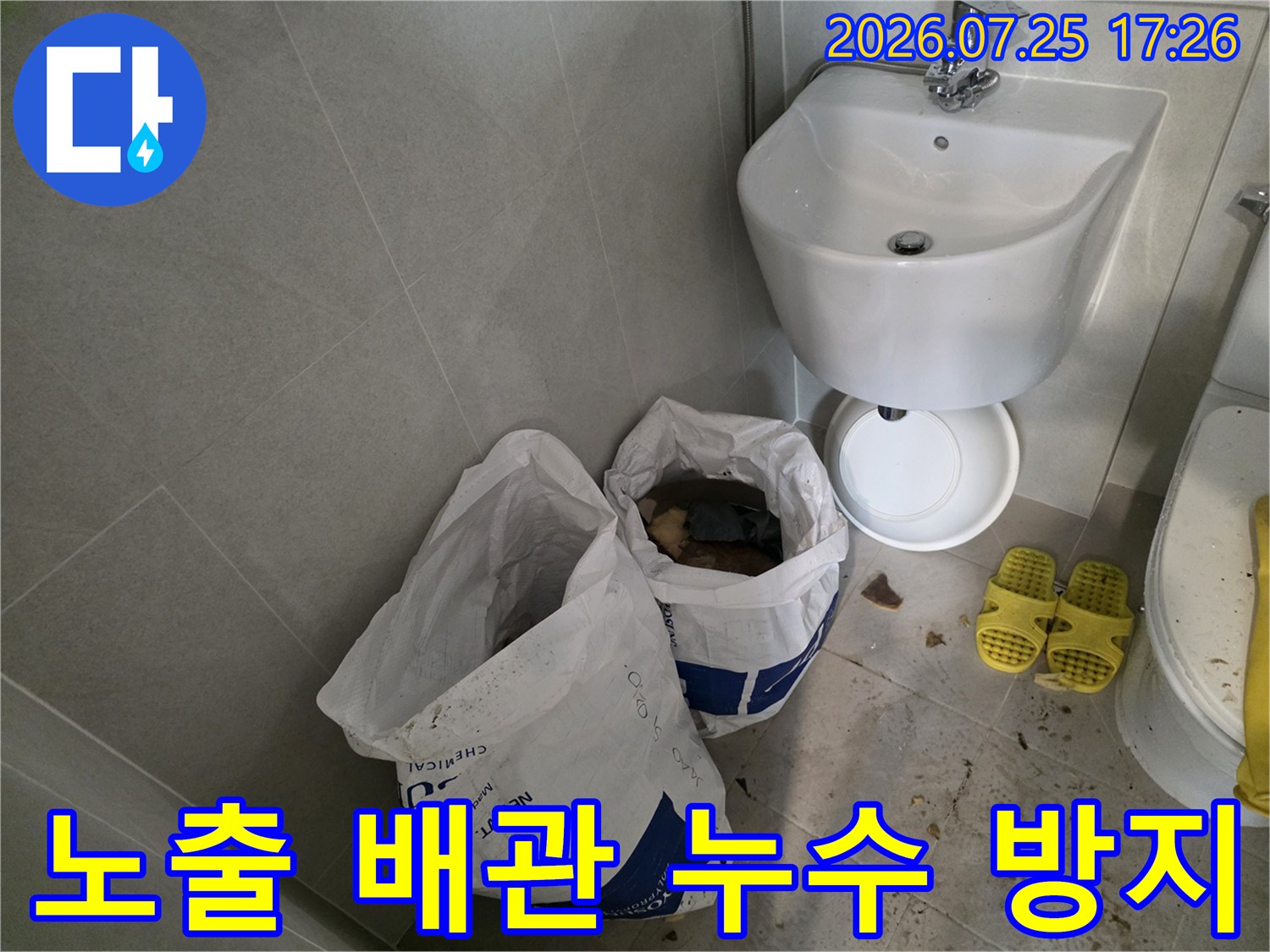화장실 세면대 밑으로 지나가는 노출 배관과 작업 용품들