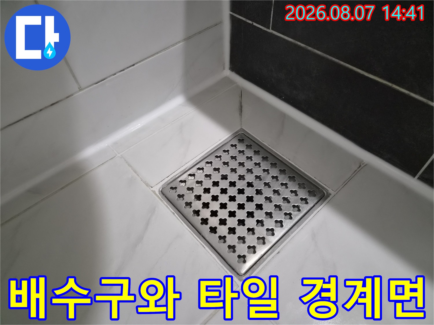 흰색 타일과 스테인리스 배수구가 만나는 지점을 촬영한 사진입니다.