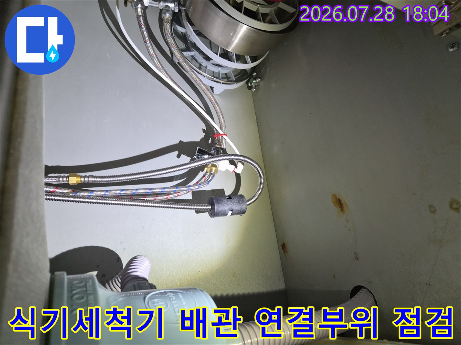 식기세척기용 급수 배관과 연결 부품이 밀집된 하부장 내부 모습