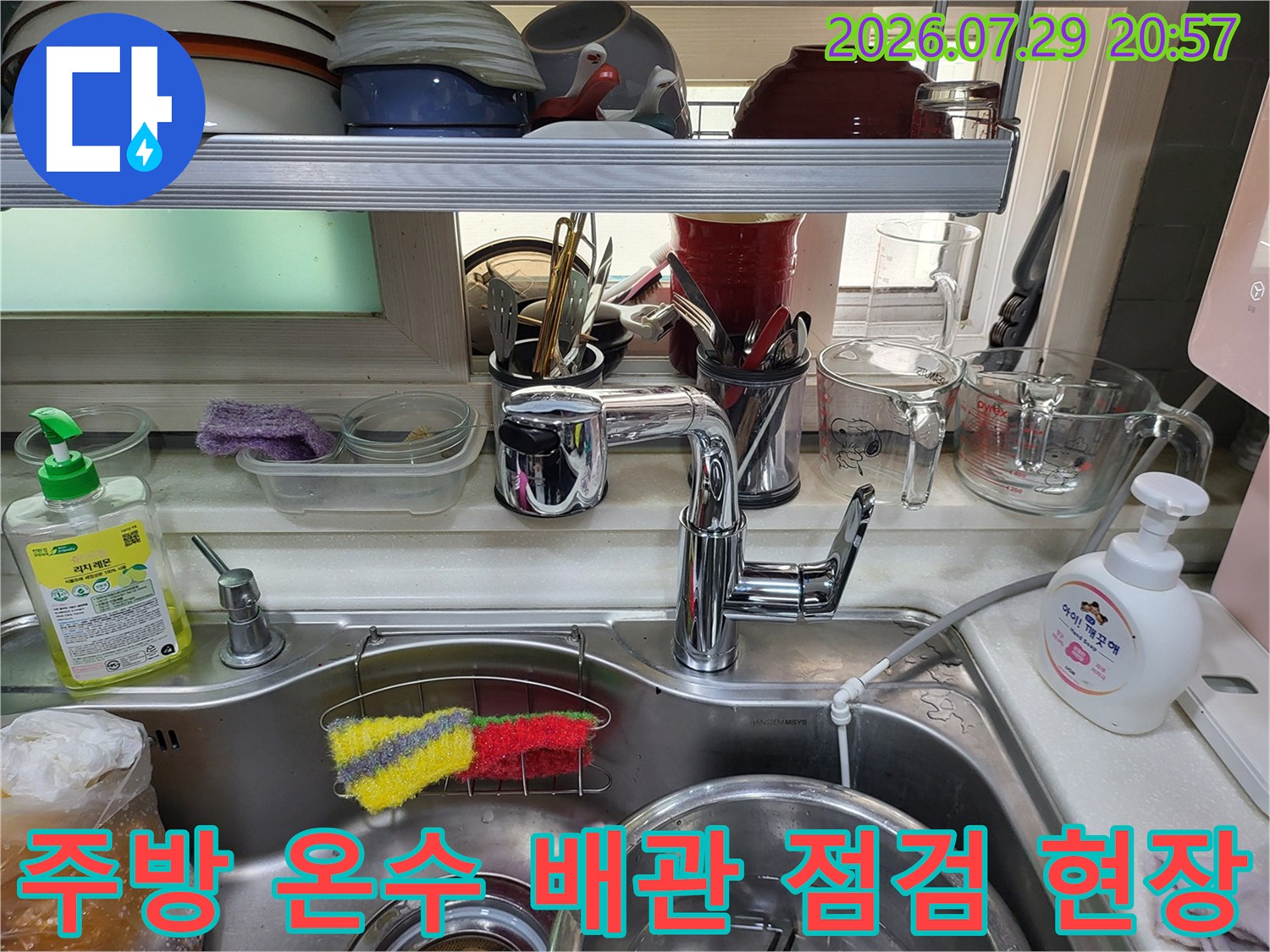 싱크대 하부의 수도 연결 부위와 세면기 구조물이 배치된 주방 공간