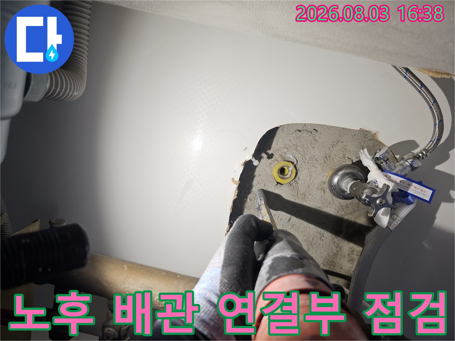 작업자가 싱크대 밑에 노출된 복잡한 배관 부위를 손으로 확인하며 점검하는 장면