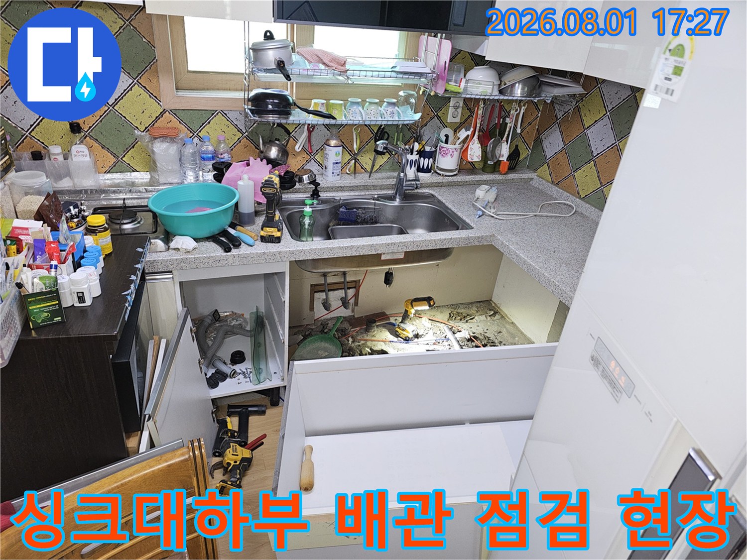 싱크대 하단부를 개방하고 바닥면의 노출된 배관과 공사 도구들을 배치한 누수 점검 현장 사진