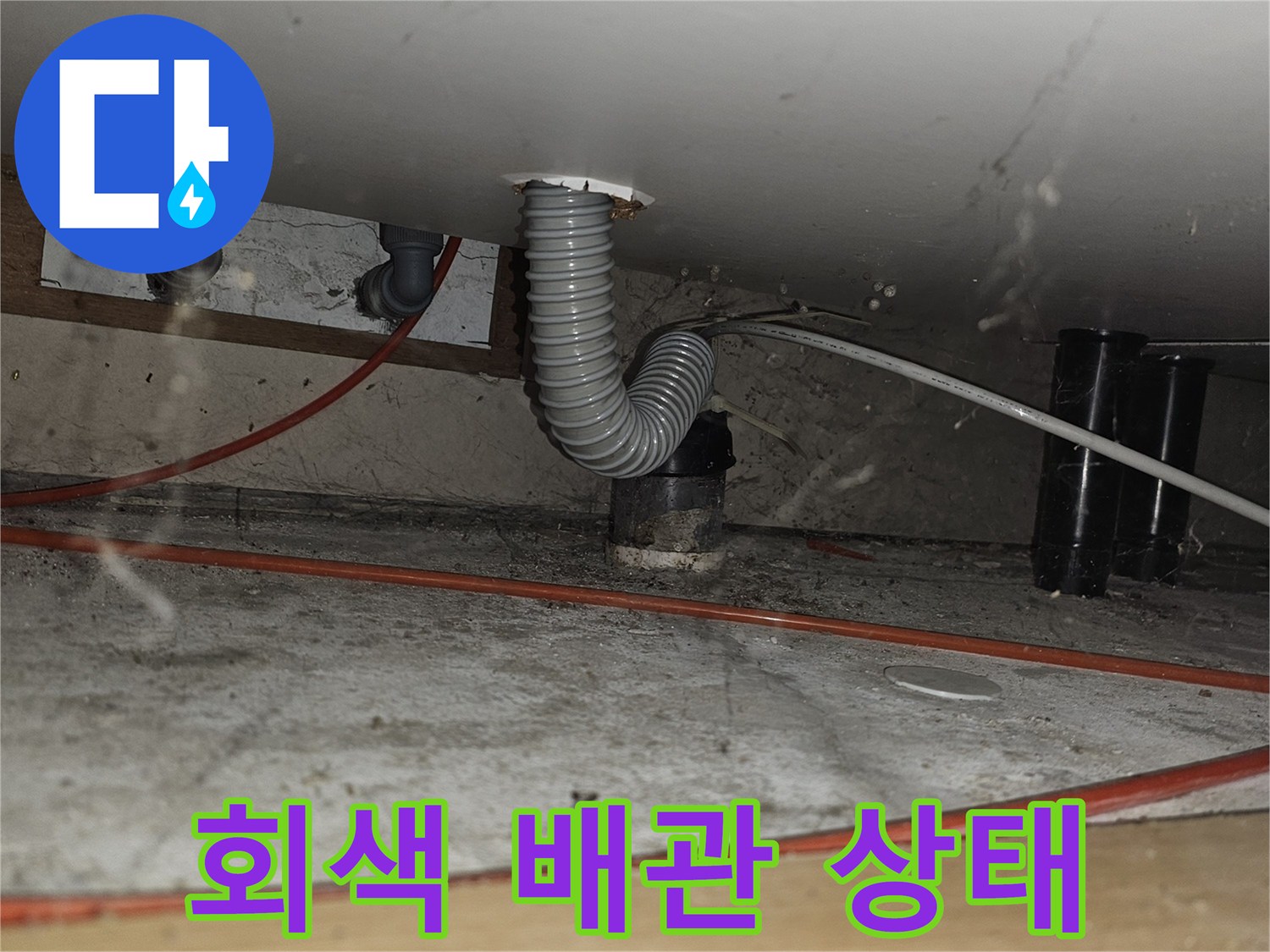 싱크대 하부-굴곡진 회색 주름관과 전기 배선