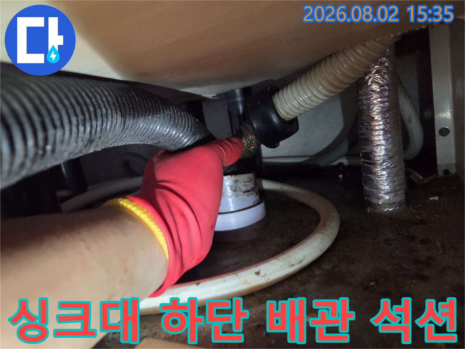 작업자가 장갑을 착용하고 싱크대 아래쪽 배수 호스와 연결된 부위에 석션기를 사용하여 이물질을 제거하는 장면.