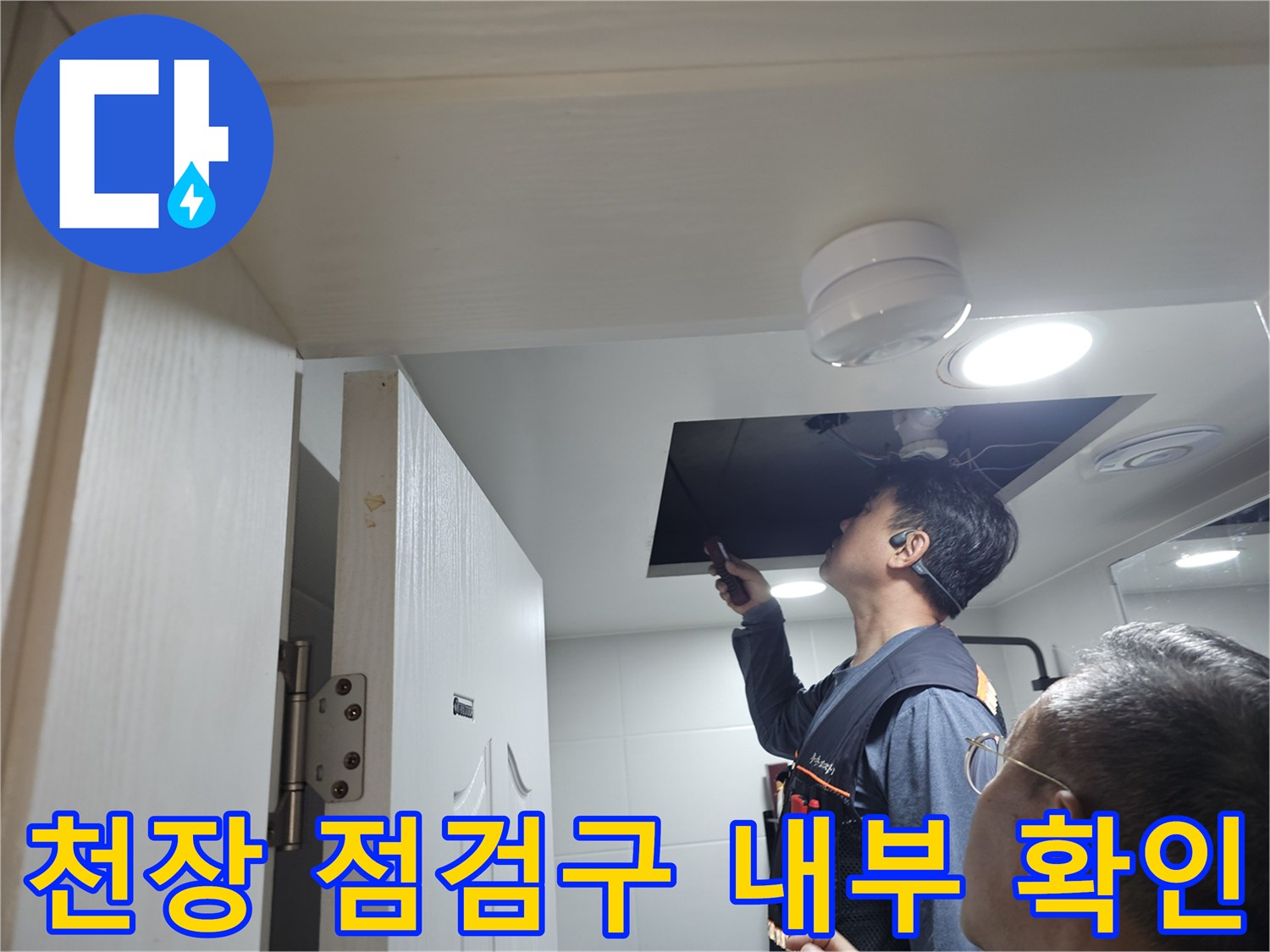 작업자가 천장 점검구를 통해 배관을 검사하는 장면