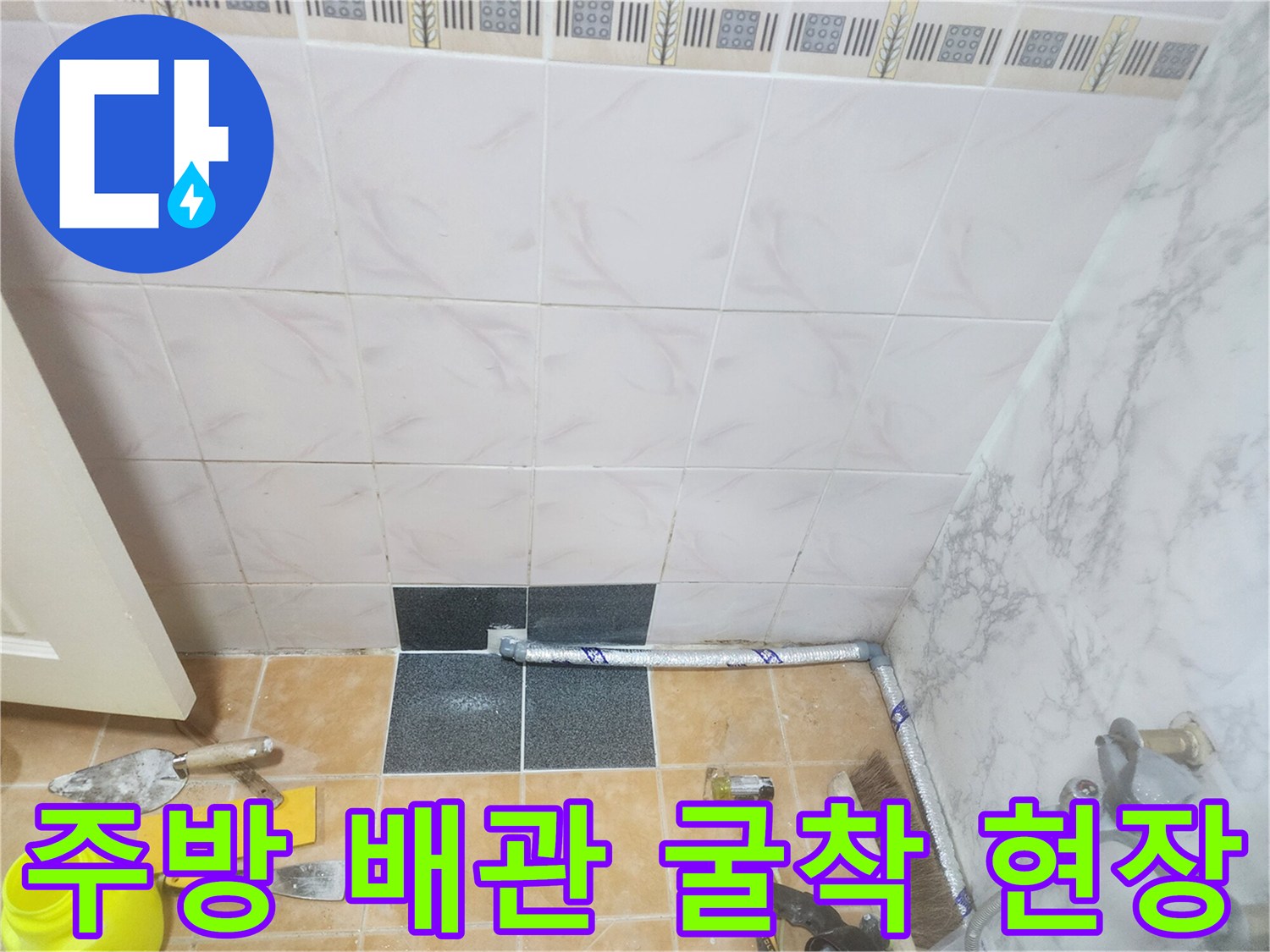 타일이 제거된 바닥에 노출된 배관과 미장 작업 도구들