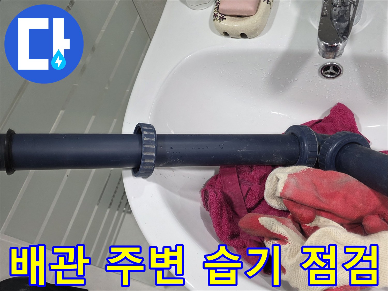 파란색 배관과 세면대 하단에 놓인 작업용 장갑 사진
