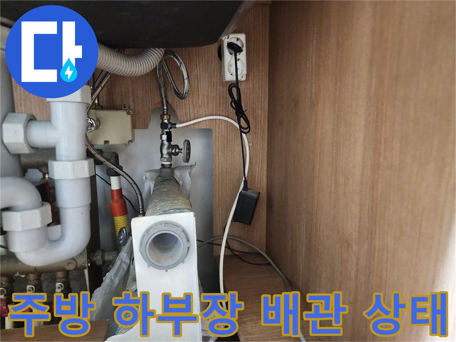 싱크대 하부의 흰색 배관과 벽면 콘센트가 포함된 모습