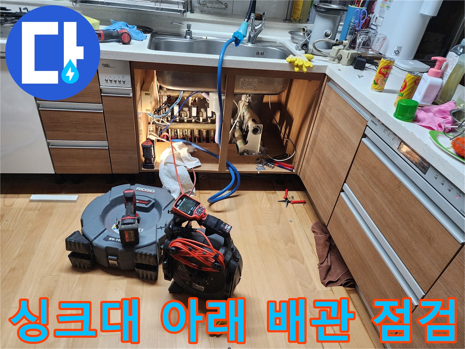주방 싱크대 하단부의 복잡한 배수 구조와 작업 도구들