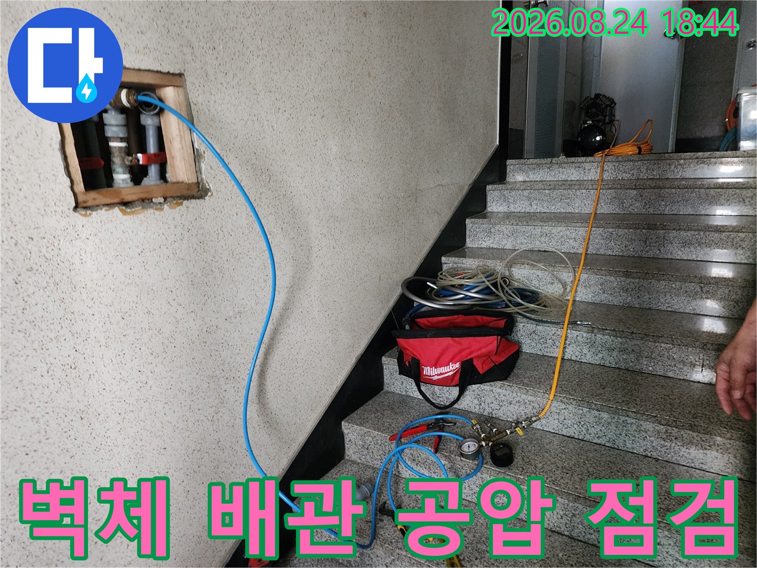 배관 연결 부위에 파란색 호스를 연결하여 압력을 측정하는 장면입니다.