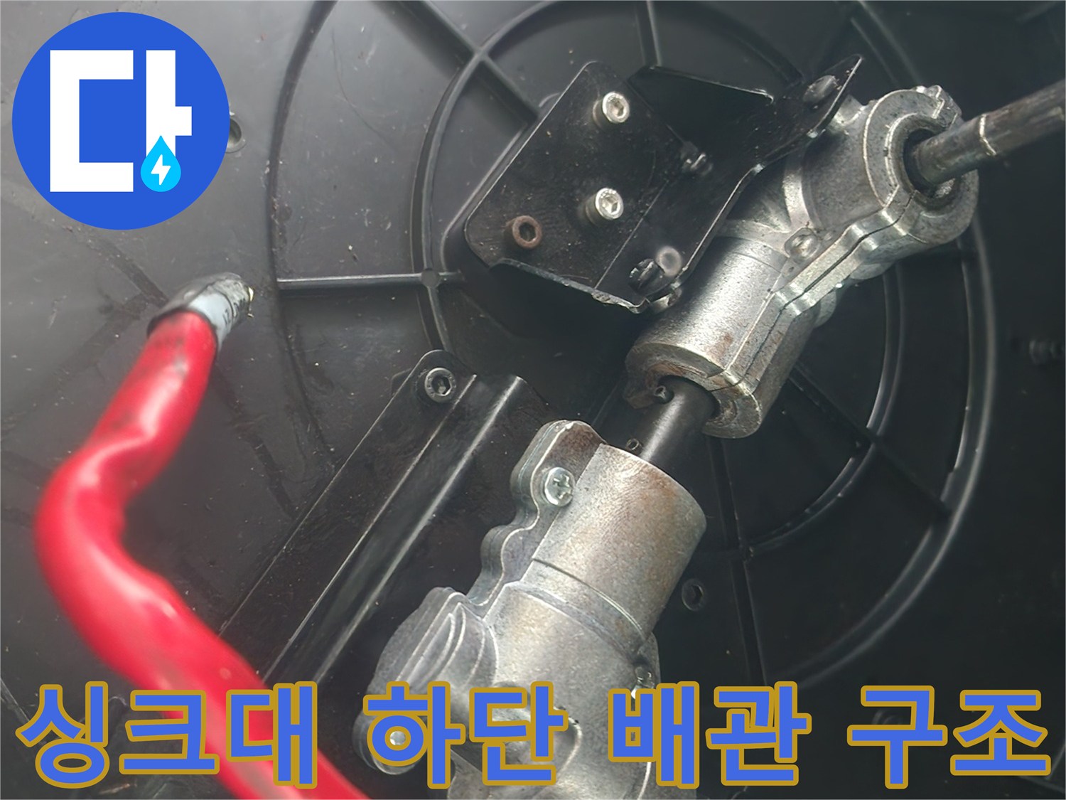 은색 금속 관과 붉은 호스가 연결된 싱크대 내부 모습