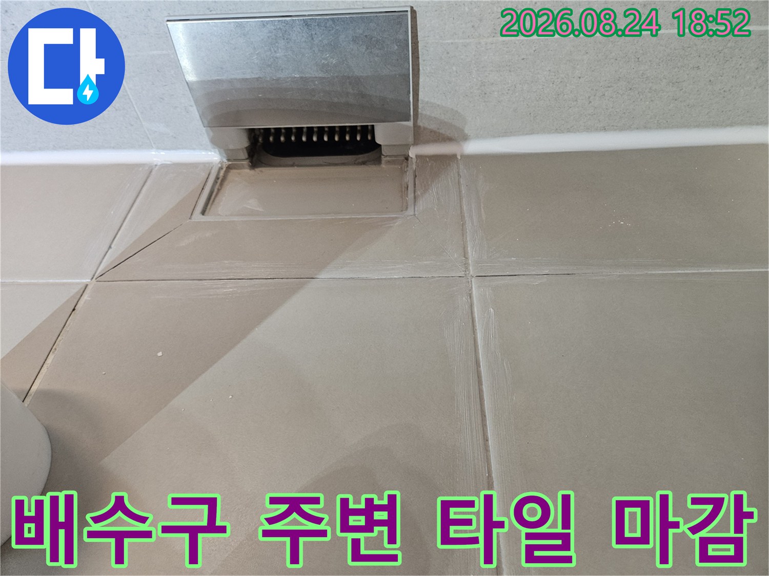 베이지색 욕실 타일과 금속 배수구 덮개가 만나는 지점의 근접 사진입니다.