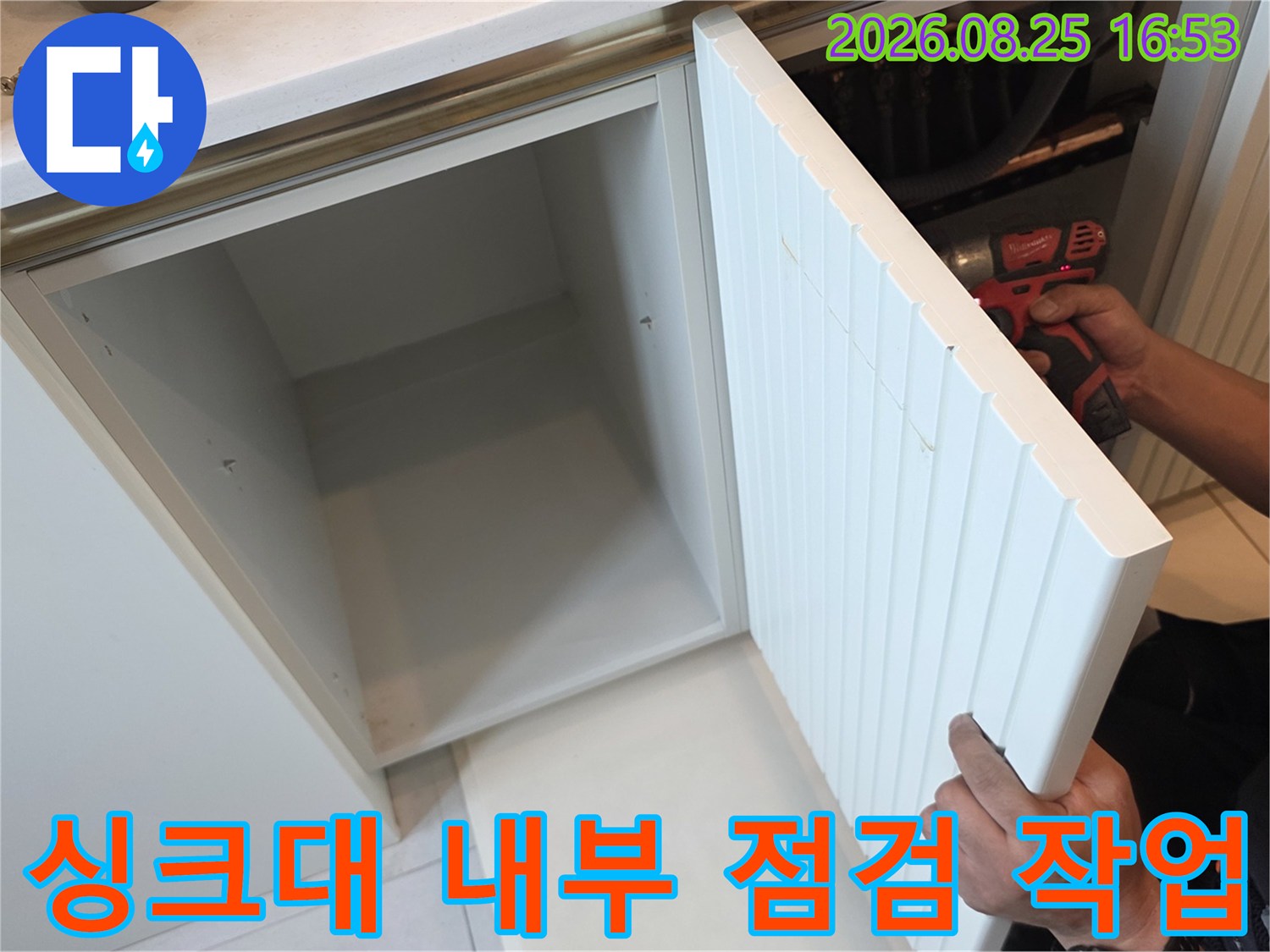 열려있는 싱크대 하부장 안쪽의 배관 연결 부위를 집중적으로 조사하고 있습니다.
