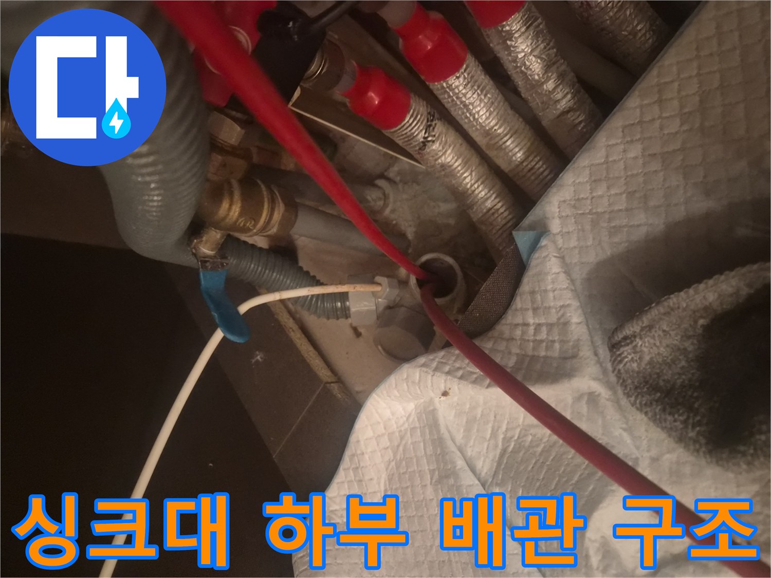 복잡한 구조의 싱크대 하단 배관과 붉은색 호스 연결 부위