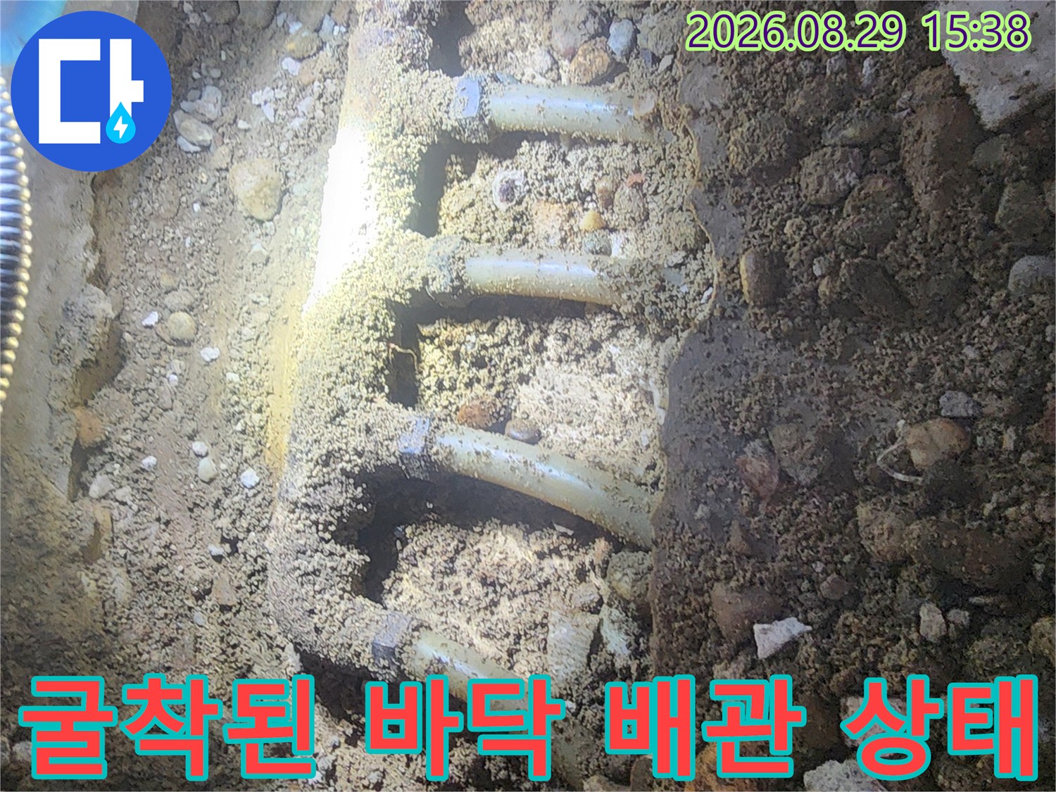 자갈과 흙 사이로 드러난 부식된 분배기 연결 배관